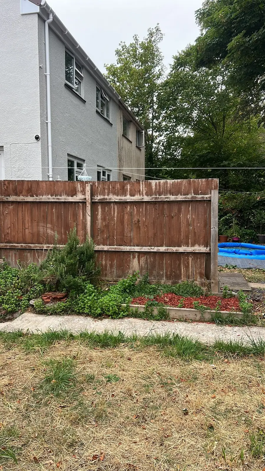 The old panel fence: peeling stain, weathered timber, and an uneven line.