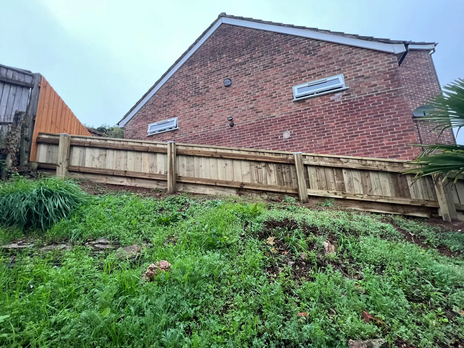 Rear of a new low closeboard fence showing posts, rails and gravel boards on a sloping lawn in Paignton