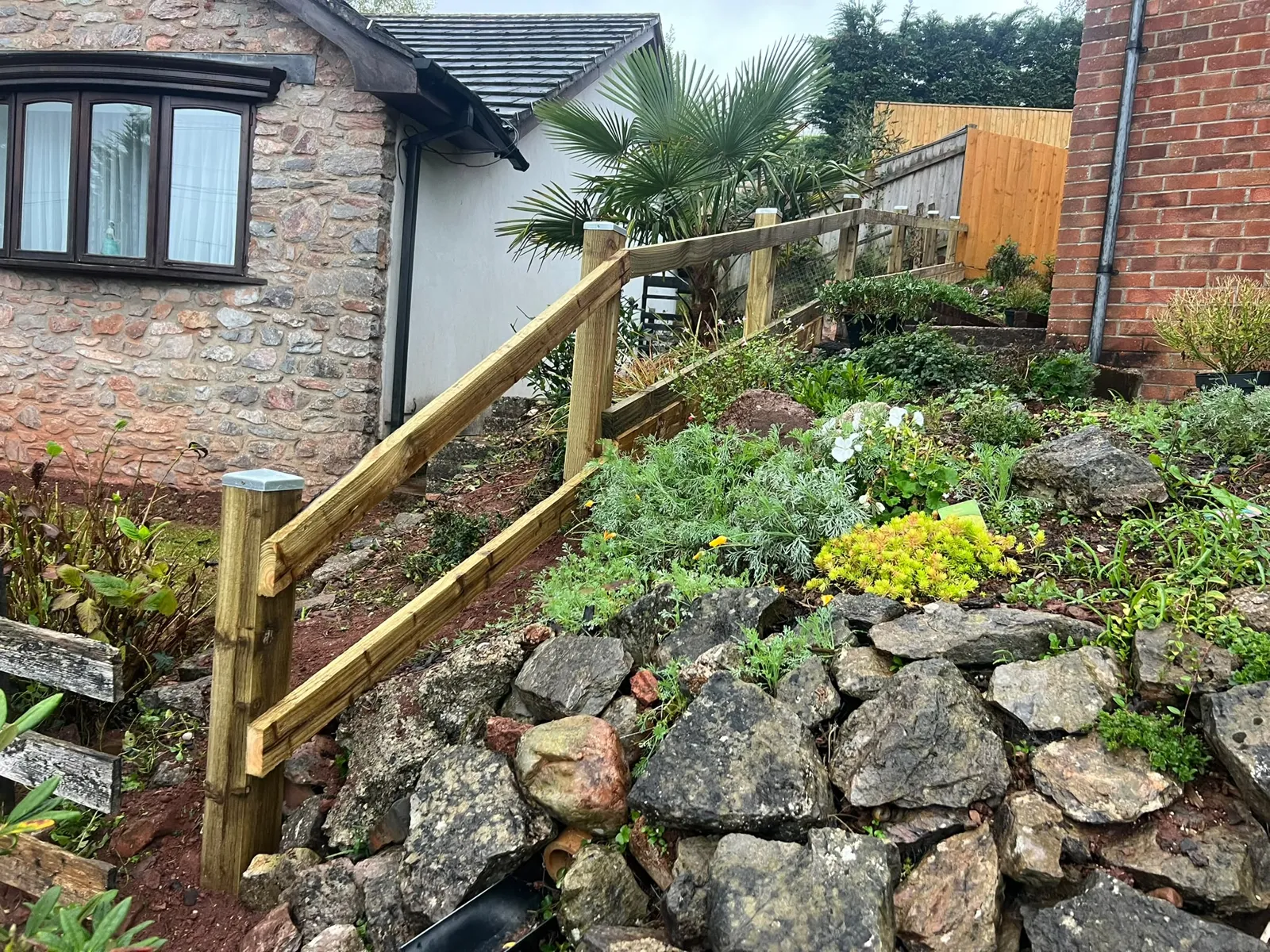 New timber posts with metal caps and rails set beside a rockery during a low fence installation in Paignton