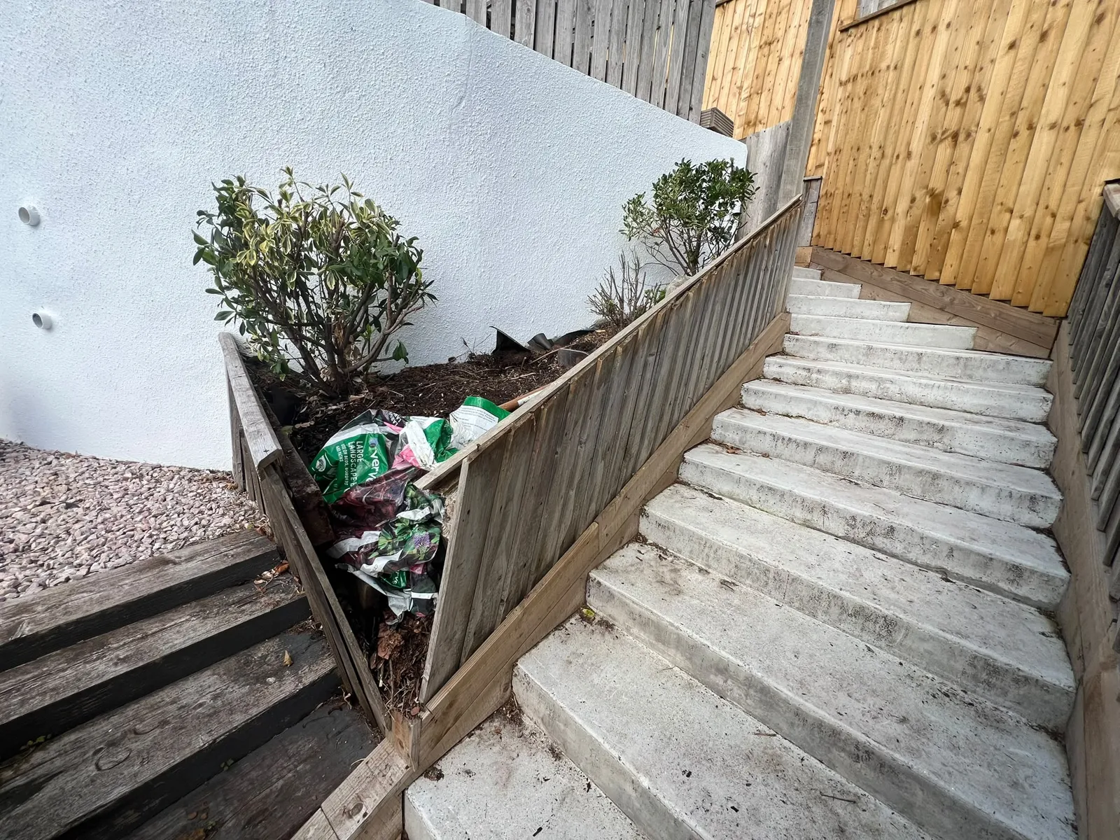 Old weathered featherboard fence leaning outwards over concrete garden steps in Paignton before replacement