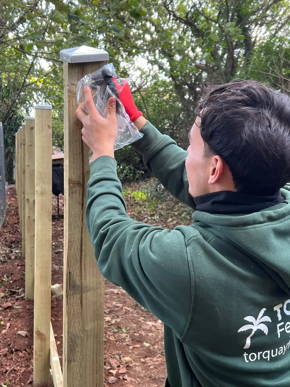 Torquay Fencing installer in a branded hoodie fitting a galvanised cap to a fence post in Wellswood, Torquay