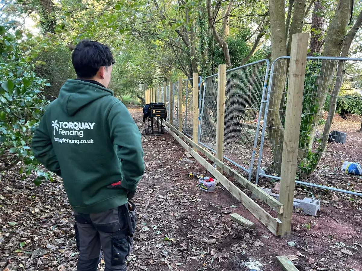 Torquay Fencing installer in a branded hoodie checking the post line on a Wellswood footpath boundary