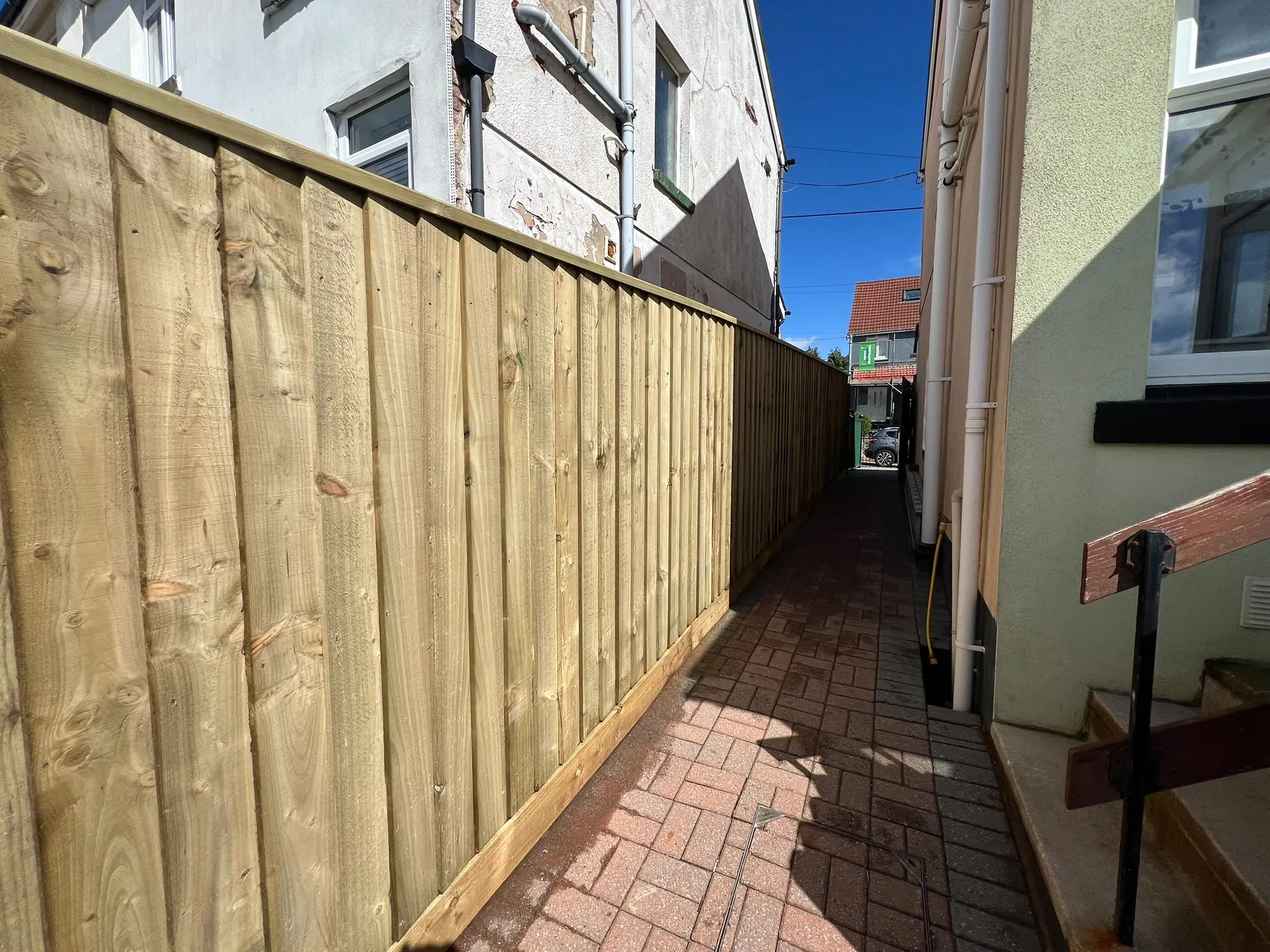 Overlapping feather-edge closeboard boards in sun along a brick alley in Paignton