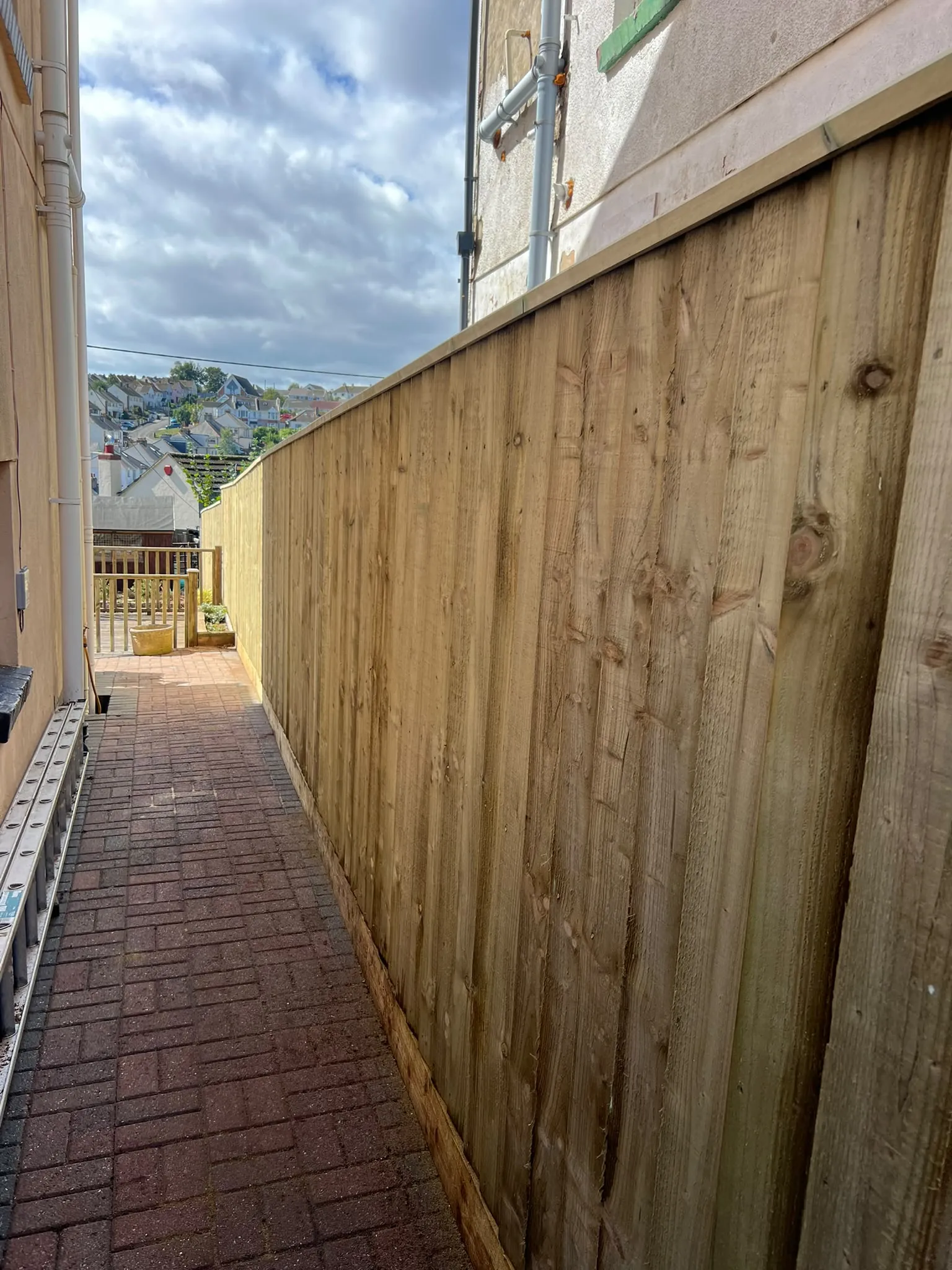 Long closeboard feather-edge fence along a narrow brick side passage in Paignton